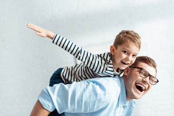 cheerful father piggybacking happy son looking at camera and imitating flying