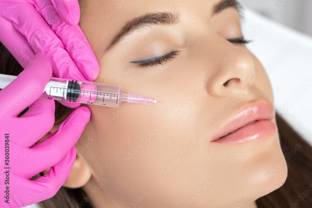 Beautiful brunette woman at the beautician.Cosmetologist does anti wrinkle injections on the face and on cheekbone. Women's cosmetology in the beauty salon. Beautiful brunette woman at the beautician.Cosmetologist does anti wrinkle injections on the face and on cheekbone. Women's cosmetology in the beauty salon.