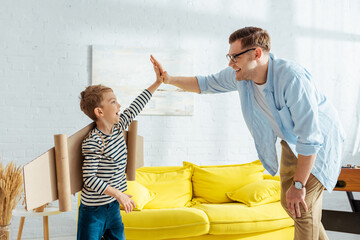 cute boy with cardboard plane wings on back giving high five to father