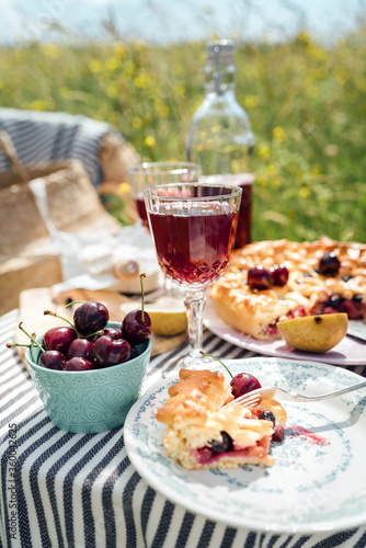 Table in garden served with beautiful vintage wine glasses, plates, silver cutlery and tableware, tablecloth, sweet cherry pie and fresh cherries still life. Homemade baking and recipes illustration.