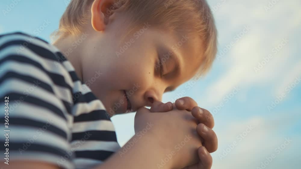 boy prays against a blue sky. child close-up concept faith religion and happy family. kid son jew crossed arms praying to god. worship and gratitude for life and a happy childhood. lifestyle catholic boy prays against a blue sky. child close-up concept faith religion and happy family. kid son jew crossed arms praying to god. worship and gratitude for life and a happy childhood. lifestyle catholic