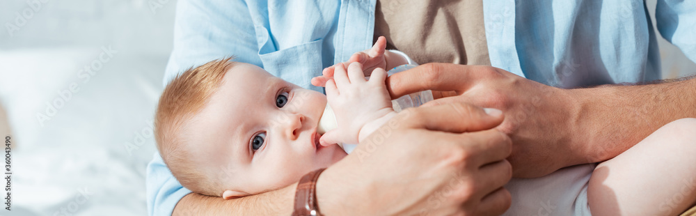 partial view of father feeding son with milk from baby bottle, horizontal image partial view of father feeding son with milk from baby bottle, horizontal image