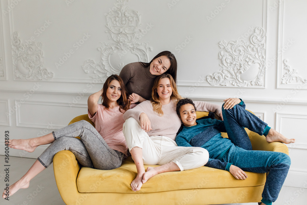 four beautiful cheerful girlfriends are sitting on the sofa in the white room at home. Four sisters four beautiful cheerful girlfriends are sitting on the sofa in the white room at home. Four sisters