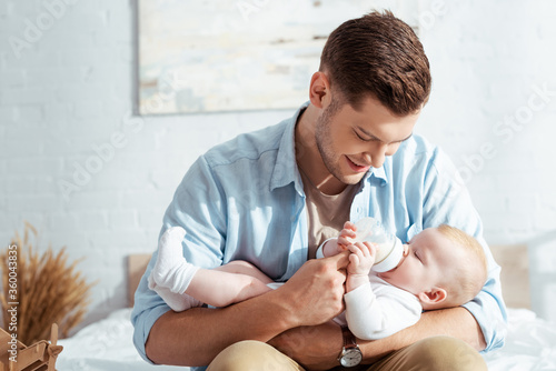 Bild auf Leinwand happy young father feeding cute baby boy with milk from baby bottle