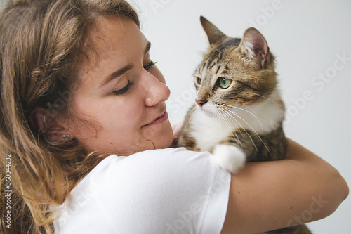 Girl is petting cat with big green eyes and lovely look at him. Pet lover on white background with domestic animal concept at home. Woman hugging domestic animal.