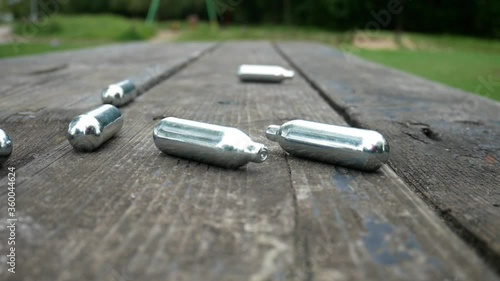Multiple metallic nitrous oxide gas cylinder recreational drug slow motion on wooden park table dolly left