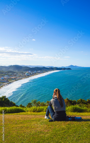 Woman contemplating the panoramic beach view from the top of the mountain. View from Praia dos Anjos, Itajai, Santa Catarina, Brazil. Touristic destination in South America.