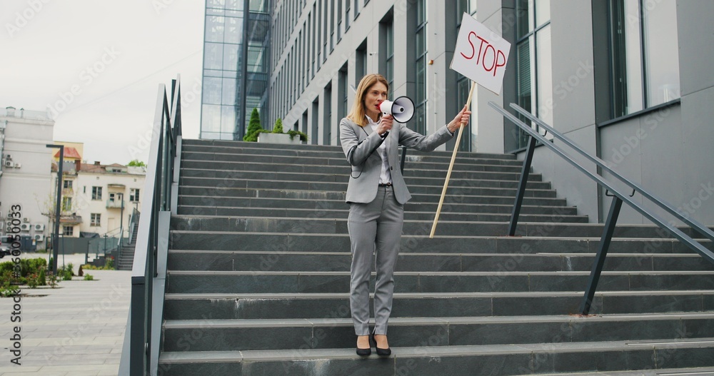 Single protest of Caucasian woman in glasses talking and screaming in megaphone. Female protestant holding table Stop while bringing attention to political or environmental issue. Lonely protestation. Single protest of Caucasian woman in glasses talking and screaming in megaphone. Female protestant holding table Stop while bringing attention to political or environmental issue. Lonely protestation.