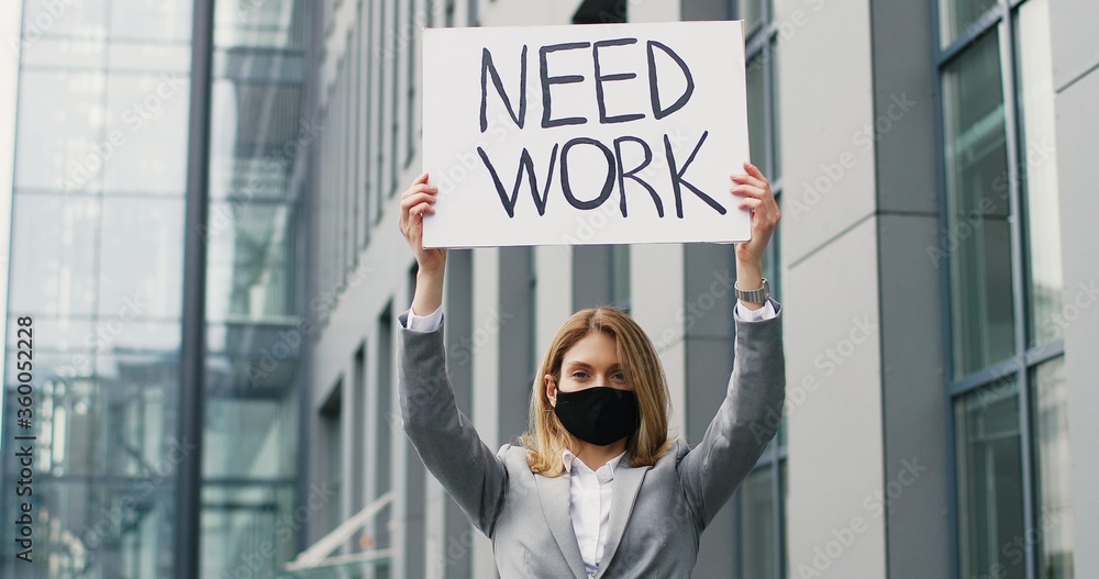 Portrait shot of Caucasian young woman demonstrating poster with words Need work. Female activist in mask showing board with looking for job announcement. Lonely protesting. Lockdown unemployment. Portrait shot of Caucasian young woman demonstrating poster with words Need work. Female activist in mask showing board with looking for job announcement. Lonely protesting. Lockdown unemployment.