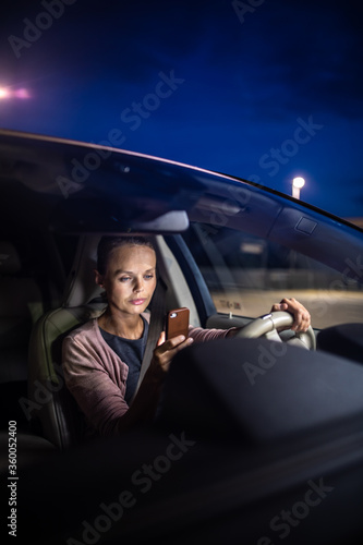 фотографія Young female driver playing with her cellphone instead of paying attention to dr