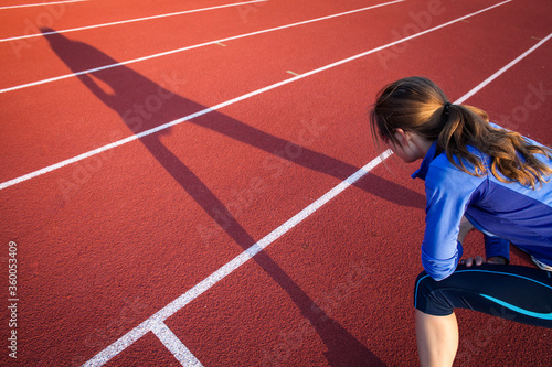 Pretty female runner stretching before her run at a track and field stadium