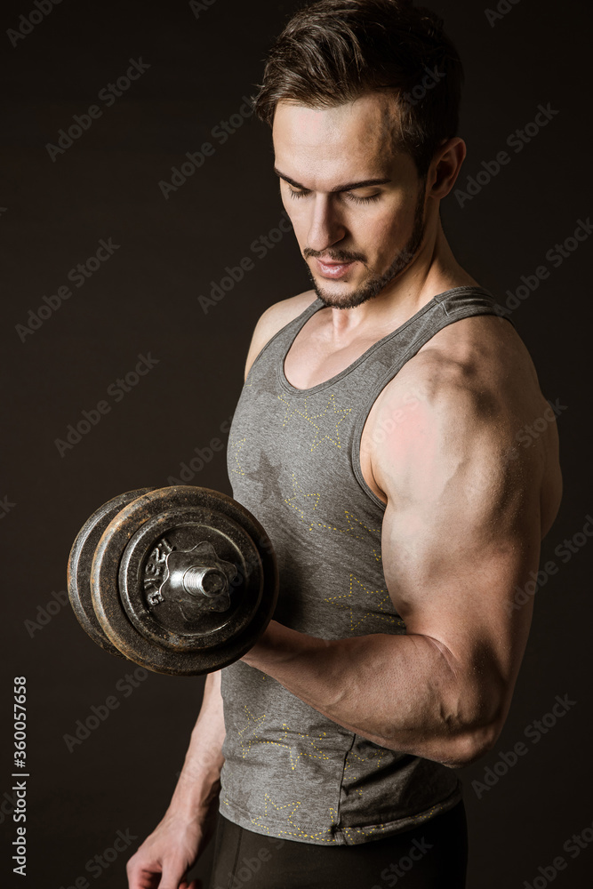 Portrait of an attractive muscular athlete with dumbbells on a dark background Portrait of an attractive muscular athlete with dumbbells on a dark background