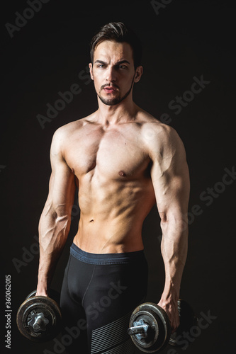 Portrait of an attractive muscular athlete with dumbbells on a dark background