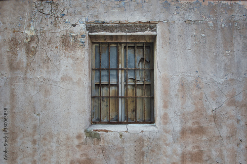 old window with broken glass on an old facadeold window with broken glass and grille on an old abandoned building