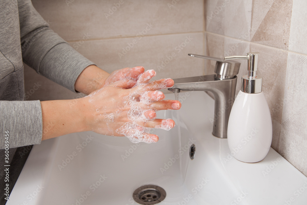 A woman washes her hands with soap over a washstand under a jet of running water. Bathroom. A woman washes her hands with soap over a washstand under a jet of running water. Bathroom.
