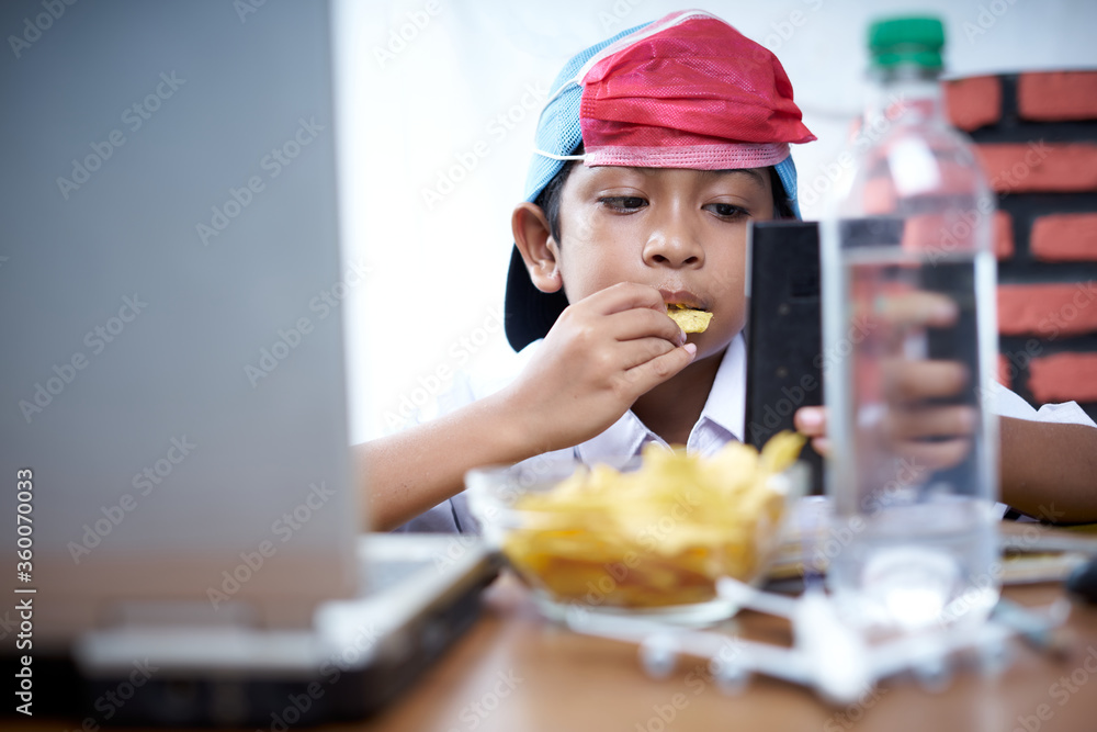 Young boy eating chips snack while study at home, New Normal Education concept Young boy eating chips snack while study at home, New Normal Education concept
