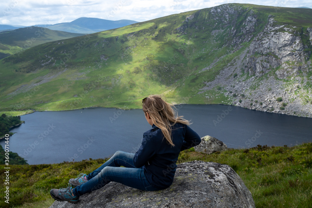 Girl (hiker) is looking at Guinness Lake (Lough Tay) -  a movie and series location, such as Vikings. Close to Dunlin City, popular tourist destination