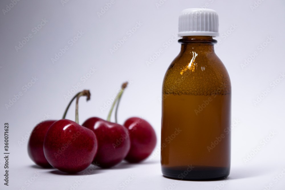 little liquid bottle with no label near cherry. body care and beauty concept. Copy space. High quality photo little liquid bottle with no label near cherry. body care and beauty concept. Copy space. High quality photo