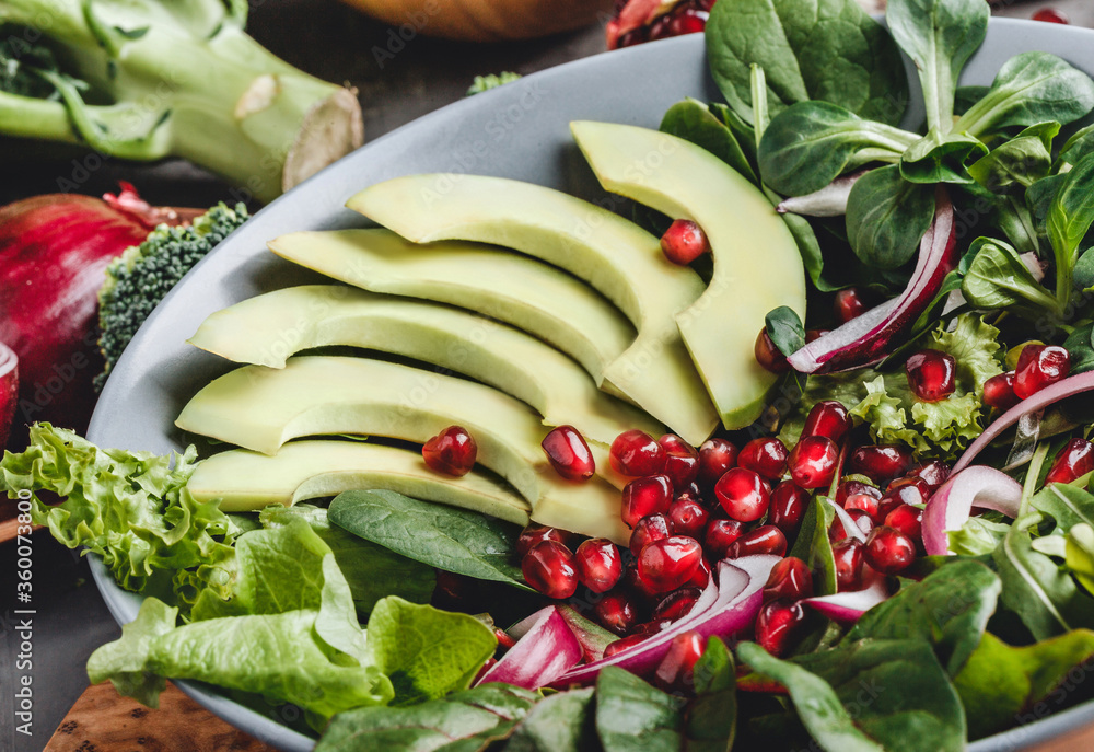 Healthy fresh salad with avocado, greens, arugula, spinach, pomegranate in plate over grey background. Healthy vegan food, clean eating, dieting, top view