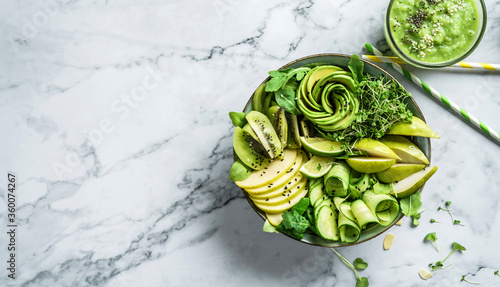 Fresh summer salad with avocado, kiwi, apple, cucumber, pear, micro greens, lime and sesame on light marble background with smoothie. Healthy food, clean eating, Buddha bowl salad, top view