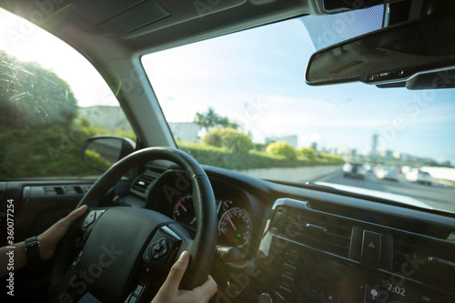 People hands holding steering wheel while driving car on city road