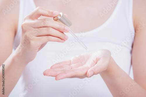 Pipette with drop of essential oil and bottle in woman hands on beige textile.