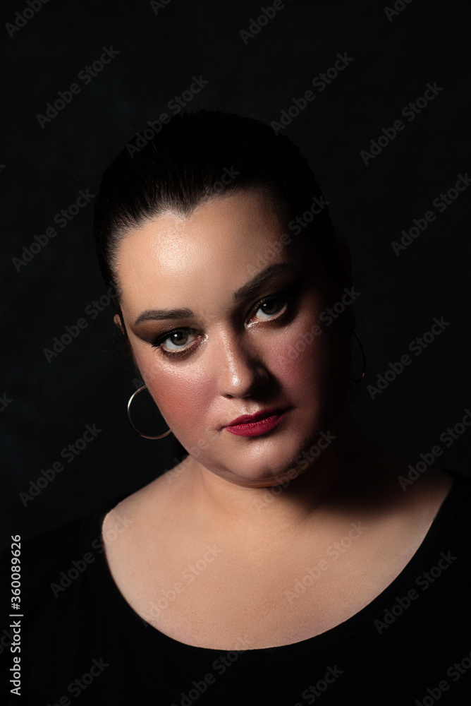 portrait of a beautiful plus-size girl. The woman looks at the camera gravely and accusingly against the dark background portrait of a beautiful plus-size girl. The woman looks at the camera gravely and accusingly against the dark background