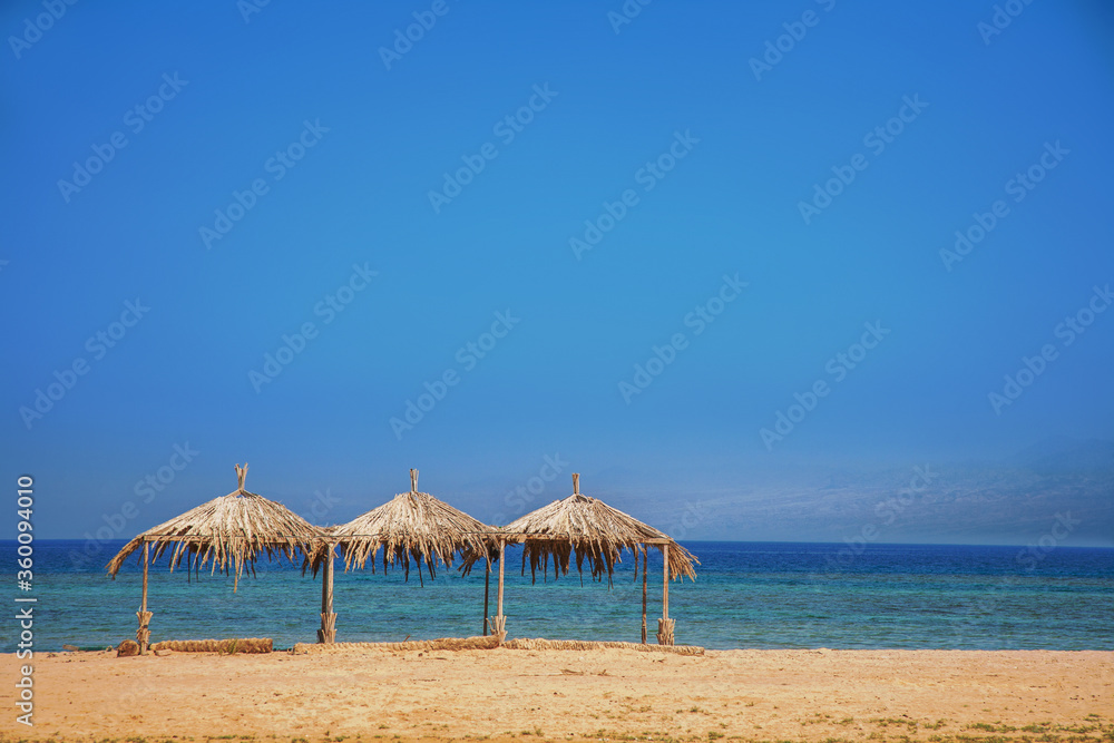 Three sunshades, made from palm leaves on the beach of the Red Sea