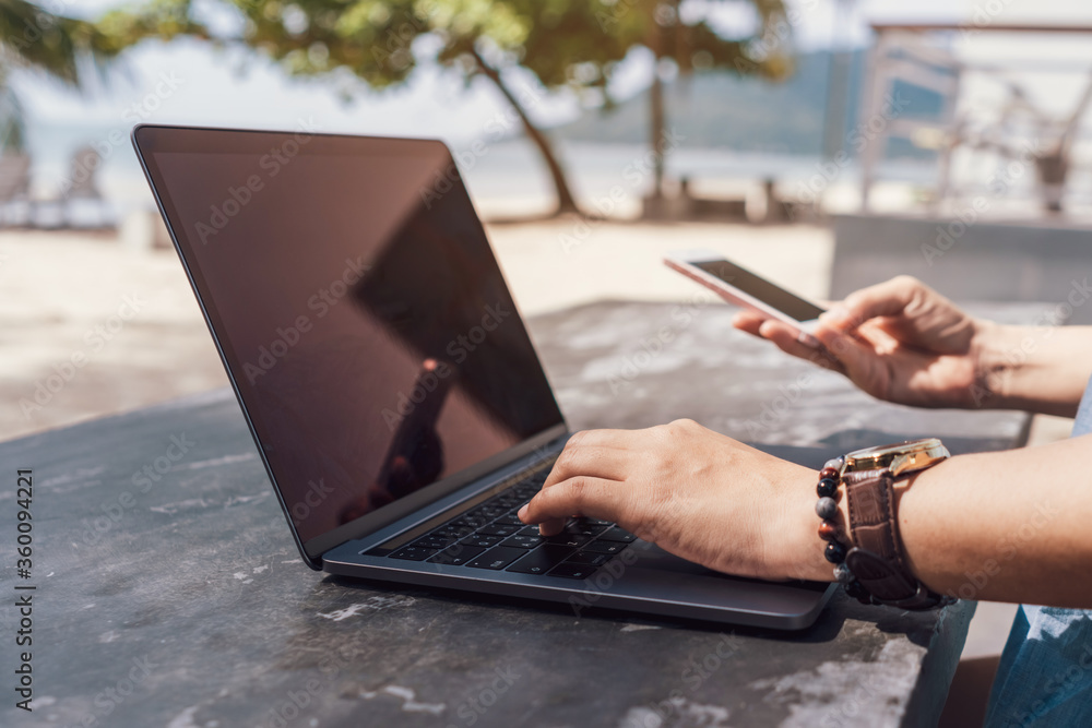 Obraz premium Woman using laptop and smartphone to work study in vacation cady at beach background.