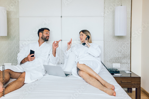 Couple in bathrobes lying and ordering room service from a hotel room