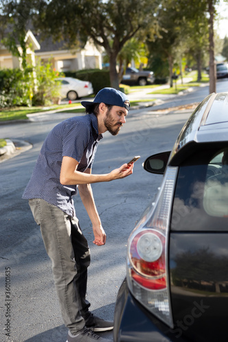 A view of a man holding a cell phone looking into the driver's side of a car, acknowledging to the driver that this vehicle is his ride share.