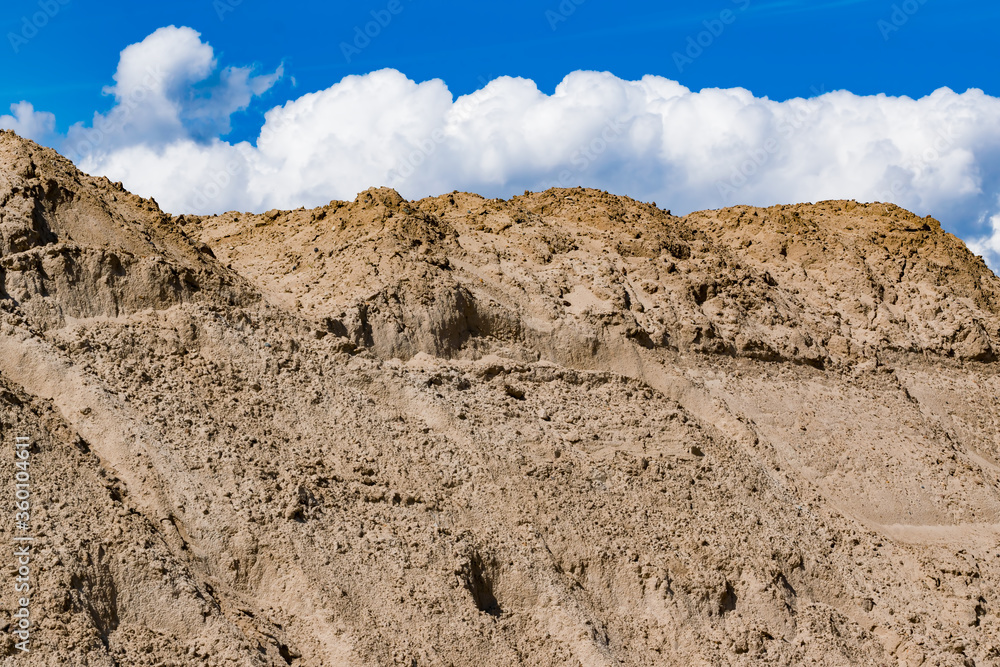 A large pile of sand for construction against a blue sky with clouds A large pile of sand for construction against a blue sky with clouds