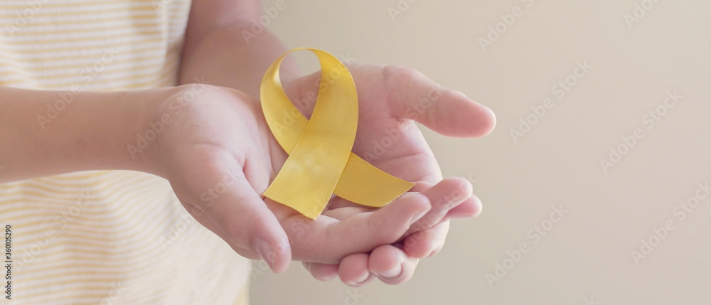 Hands holding yellow gold ribbon, Sarcoma Awareness, Bone cancer, childhood cancer awareness, September yellow, World Suicide Prevention Day concept - obrazy, fototapety, plakaty 