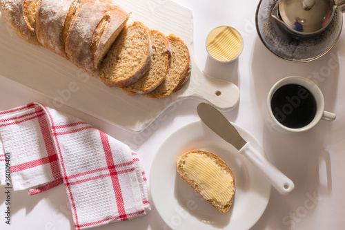 Mesa com Café da Manha: Pão Integral com manteiga, chícara de café, bule com café, toalha vermelha xadrez, pão integral fatiado sobre tábua branca, manteiga no ramequim, pão com manteiga Ponto de vist photo