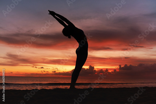 Yoga Poses. Woman Standing In Backbend Asana On Ocean Beach. Female Silhouette Practicing In Anuvittasana Pose At Beautiful Sunset. Yoga As Exercise For Lifestyle. photo