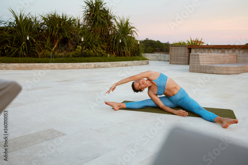 Yoga. Woman Sitting In Asana. Brunette In Blue Sportswear Practicing Mahamudra Female Stretching On Mat At Sunset. Yoga Exercising As Lifestyle. photo