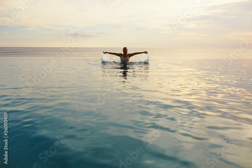 Ocean. Woman Standing In Sea. Girl Splashing Water Surface And Looking At Camera. Beautiful Seascape And Female Silhouette. Vacation In Tropical Country. © puhhha