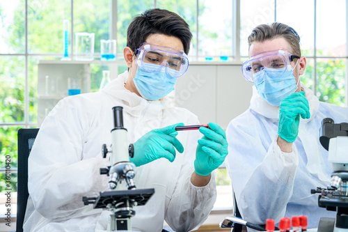 Couple male scientist wearing protection suit holding vaccine and working with many lab equipment for research vaccine at laboratory.