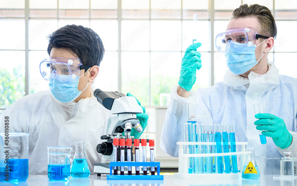 Couple male scientist wearing protection suit holding beaker or tube with sample liquid inside and working with many lab equipment for research at laboratory. Couple male scientist wearing protection suit holding beaker or tube with sample liquid inside and working with many lab equipment for research at laboratory.