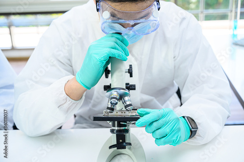 Male scientist wearing protection suit working with microscope and many lab equipment for research at laboratory.