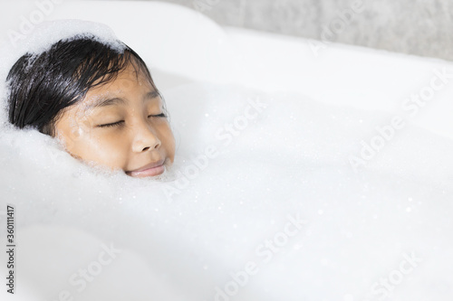 An Asian girl is happily soaking in a bubble bath.