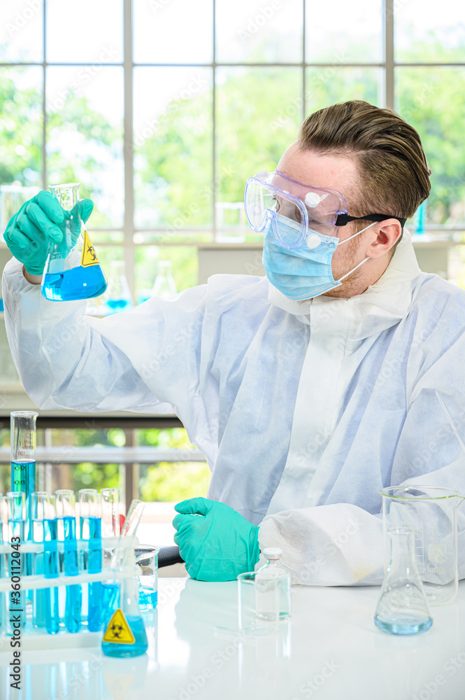Male scientist wearing protection suit holding beaker or tube with sample liquid inside and working with many lab equipment for research at laboratory. Male scientist wearing protection suit holding beaker or tube with sample liquid inside and working with many lab equipment for research at laboratory.