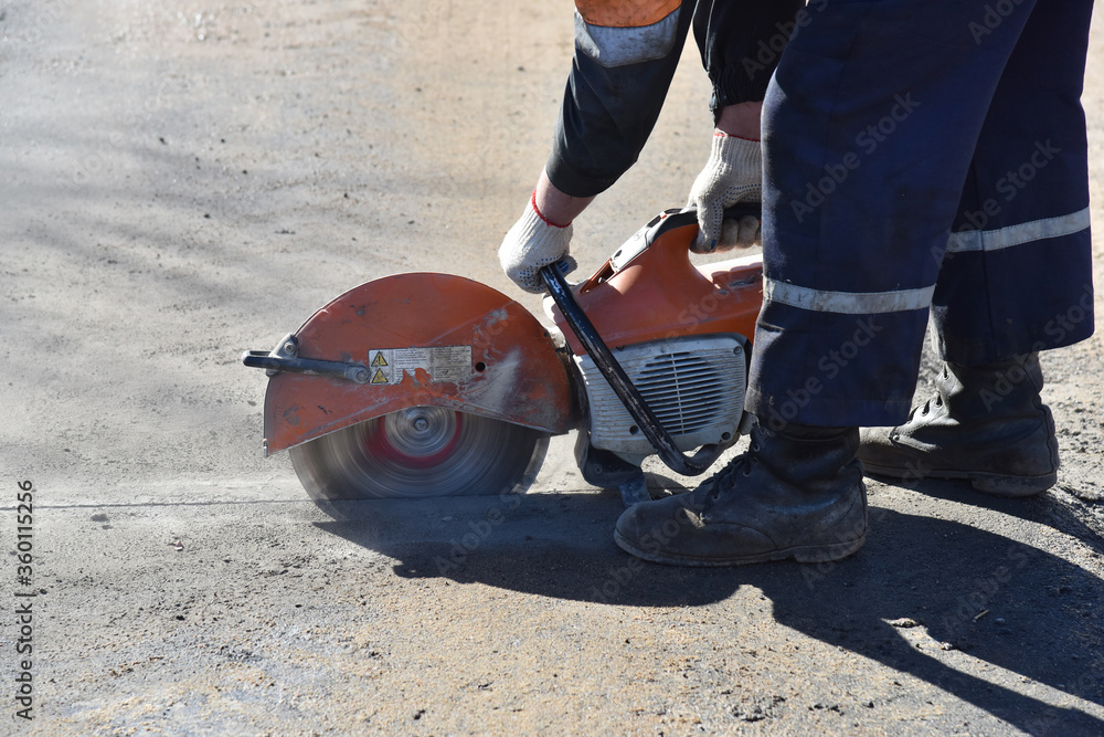 Obraz premium The builder uses a circular saw to cut part of the asphalt surface.