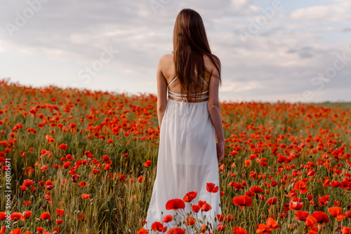 Back view of a woman in white dress walking in a red poppies field