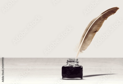 Feather quill pen and glass inkwell on desk