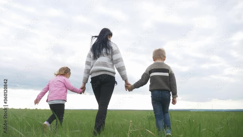 happy family. mom and little children walk in the park teamwork outdoors holding hands. woman and little boy and girl walk on a green field at lifestyle sunset happy family. mom and little children walk in the park teamwork outdoors holding hands. woman and little boy and girl walk on a green field at lifestyle sunset