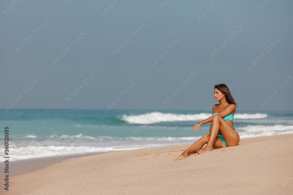 Side view of female in bikini sitting at the beach. Caucasian woman resting on the beach on a summer day Side view of female in bikini sitting at the beach. Caucasian woman resting on the beach on a summer day