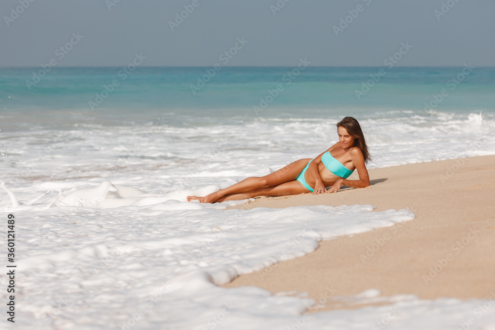 Attractive brunette girl take sunbath on the beach, happy female wearing stylish colorful swimwear, enjoying summer holidays