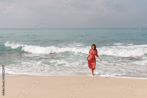 Summer vacation. Lifestyle portrait young woman relax and chill on beach background. Woman wearing red dress fashion summer trips walking enjoy tropical beach. Lifestyle and Travel Concept.