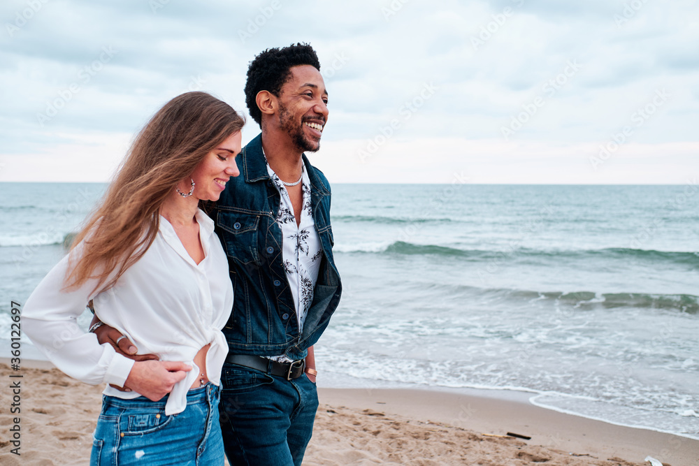 young interracial couple at the beach taking a walk